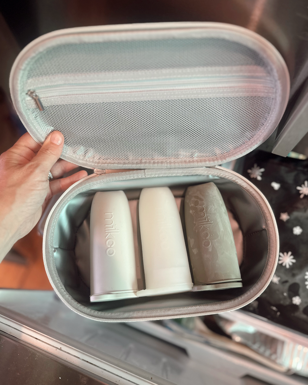 Insulated Travel case with breast milk storage pods inside, held by a hand on a reflective surface.